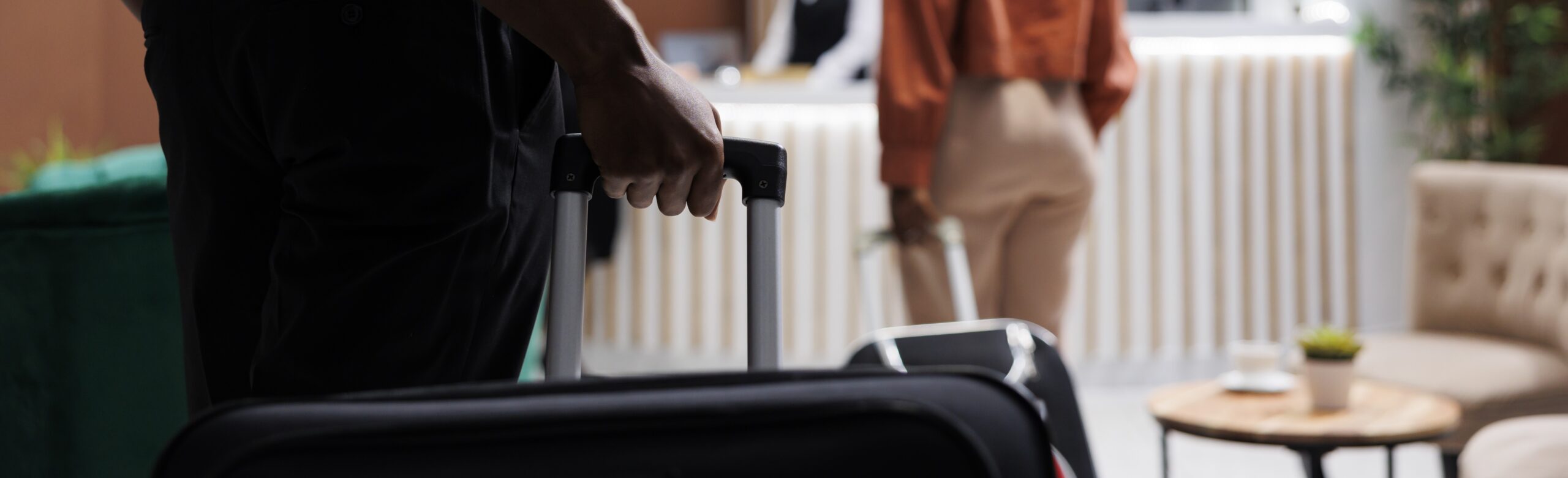 African american man carrying bags in hotel lobby, arriving at reception counter with woman to check in. Guests preparing to fill in registration forms, staff welcoming tourists.